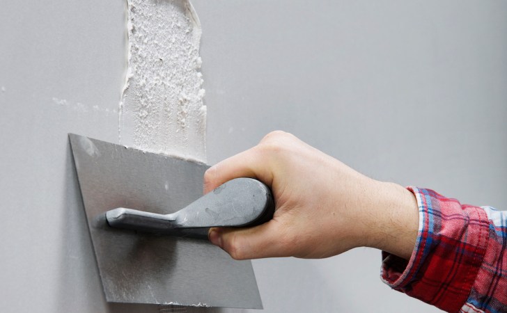 A person is repairing a white plaster wall with a plaster trowel.