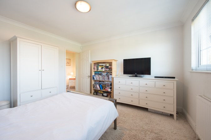 A view of a double bedroom interior with white walls, a dresser, and a bookshelf.