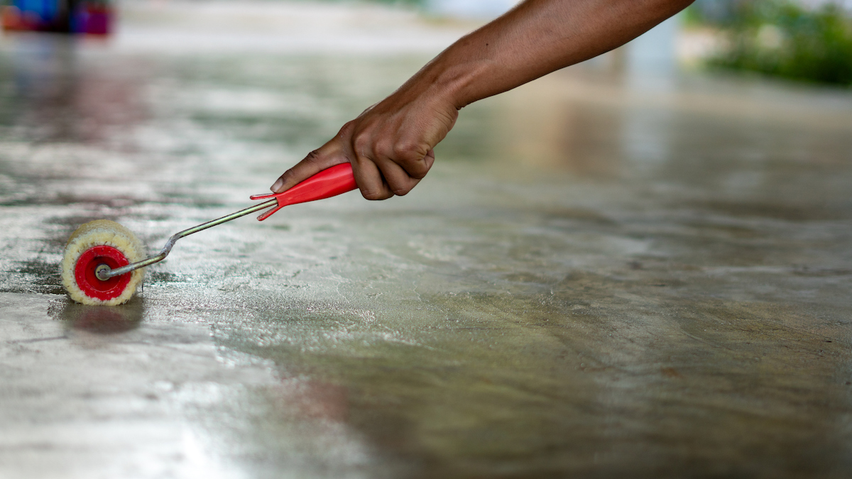 Person uses paint roller to apply a coat of lacquer to a concrete floor.