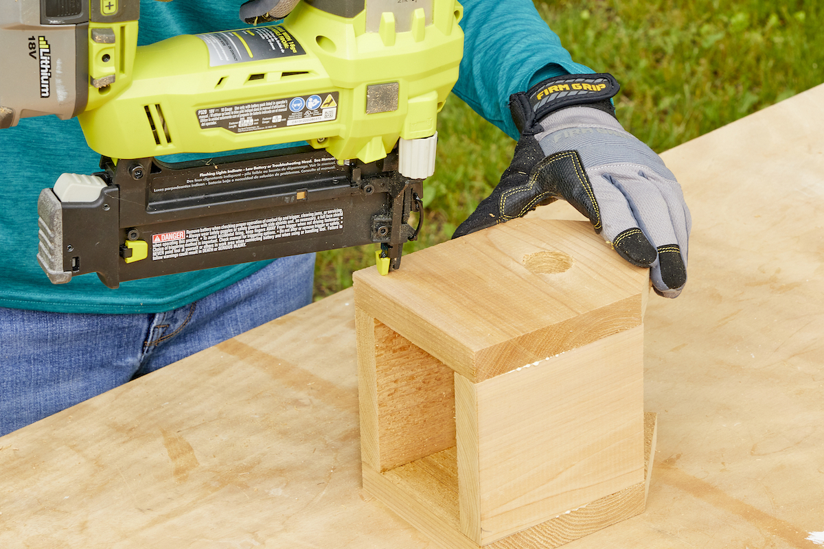 Woman nails the front of a birdhouse onto the rest of the structure.