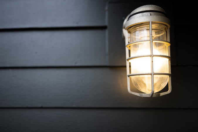 Illuminated natuical-style outdoor sconce on a house with dark grey siding.