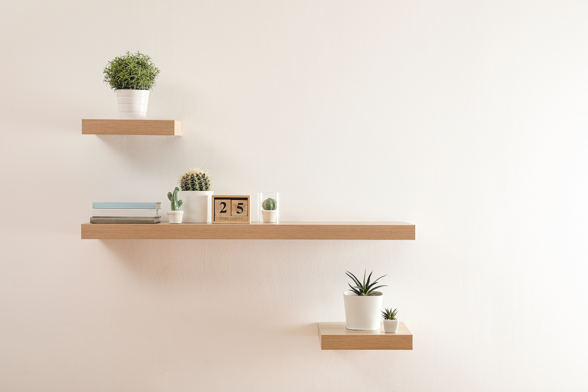 Wooden floating shelves with plants and calendar on a light-colored wall.