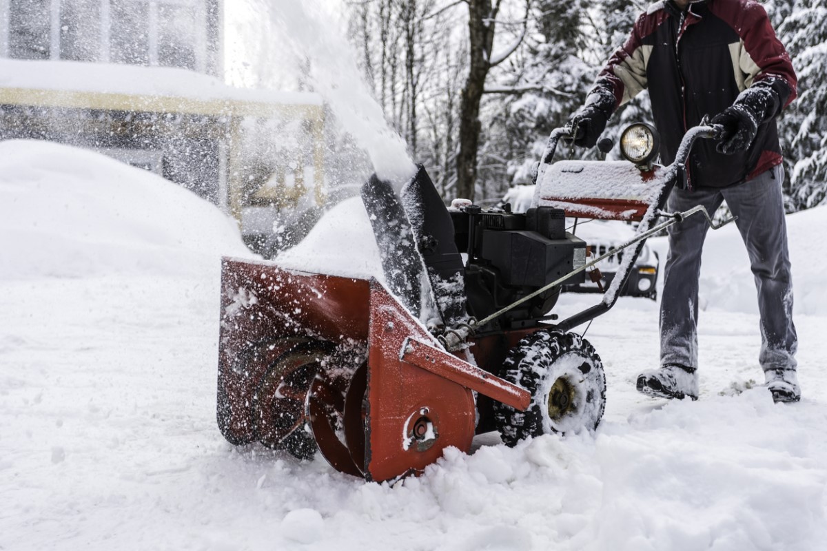 Person wearing winter clothing pushing a snow blower through a snowy driveway.