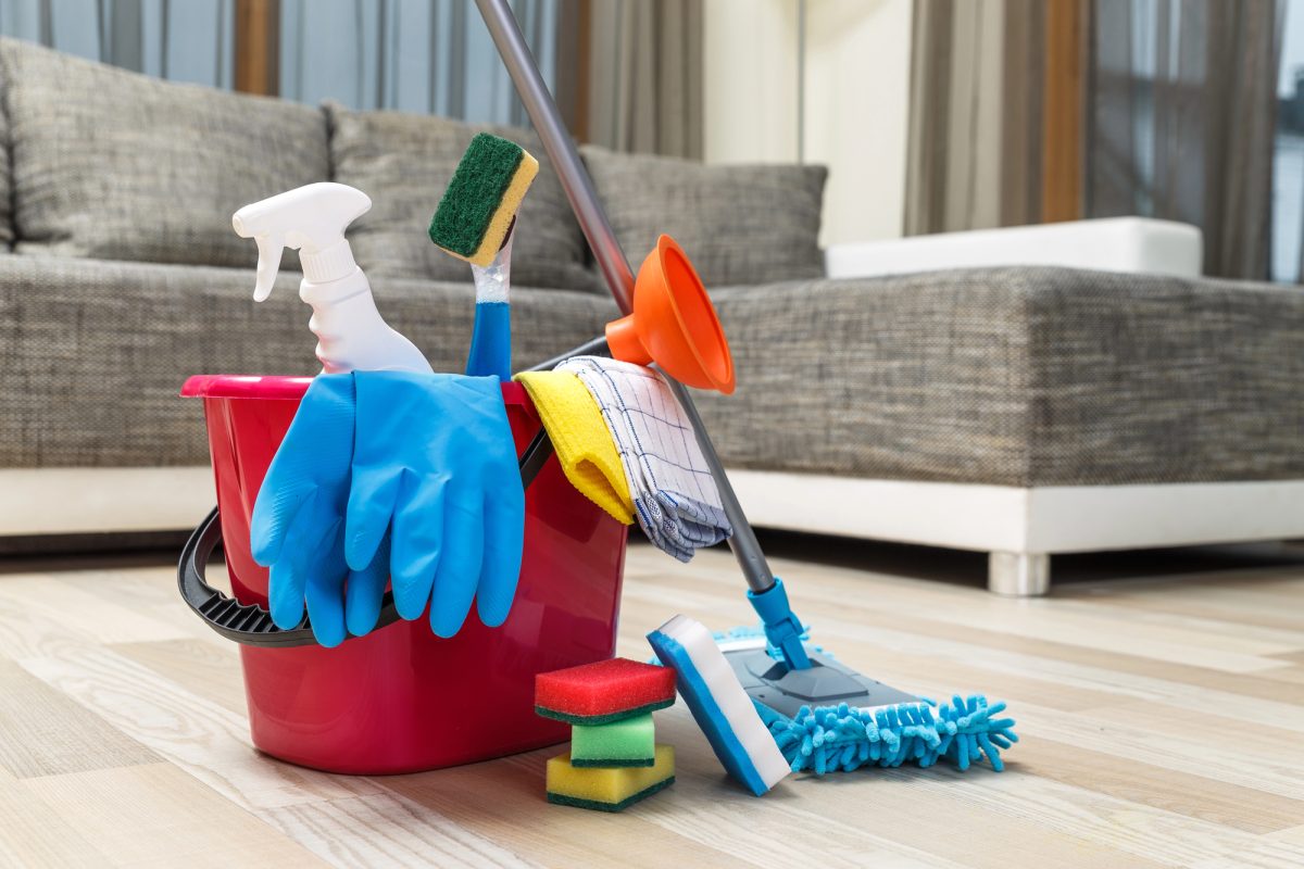 A mop and stack of sponges are leaned against a bucket filled with gloves and cleaning supples.