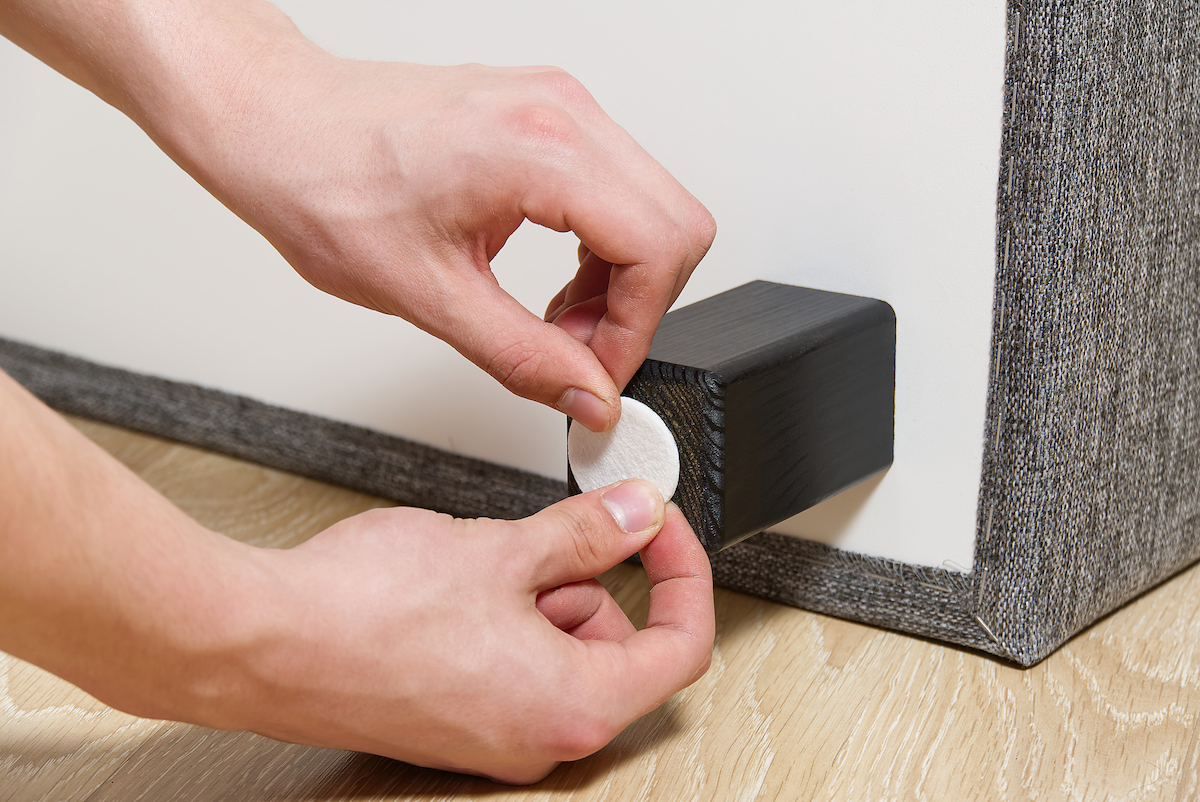 A person is sticking a circular felt furniture pad to the bottom of the leg of a table or chair.