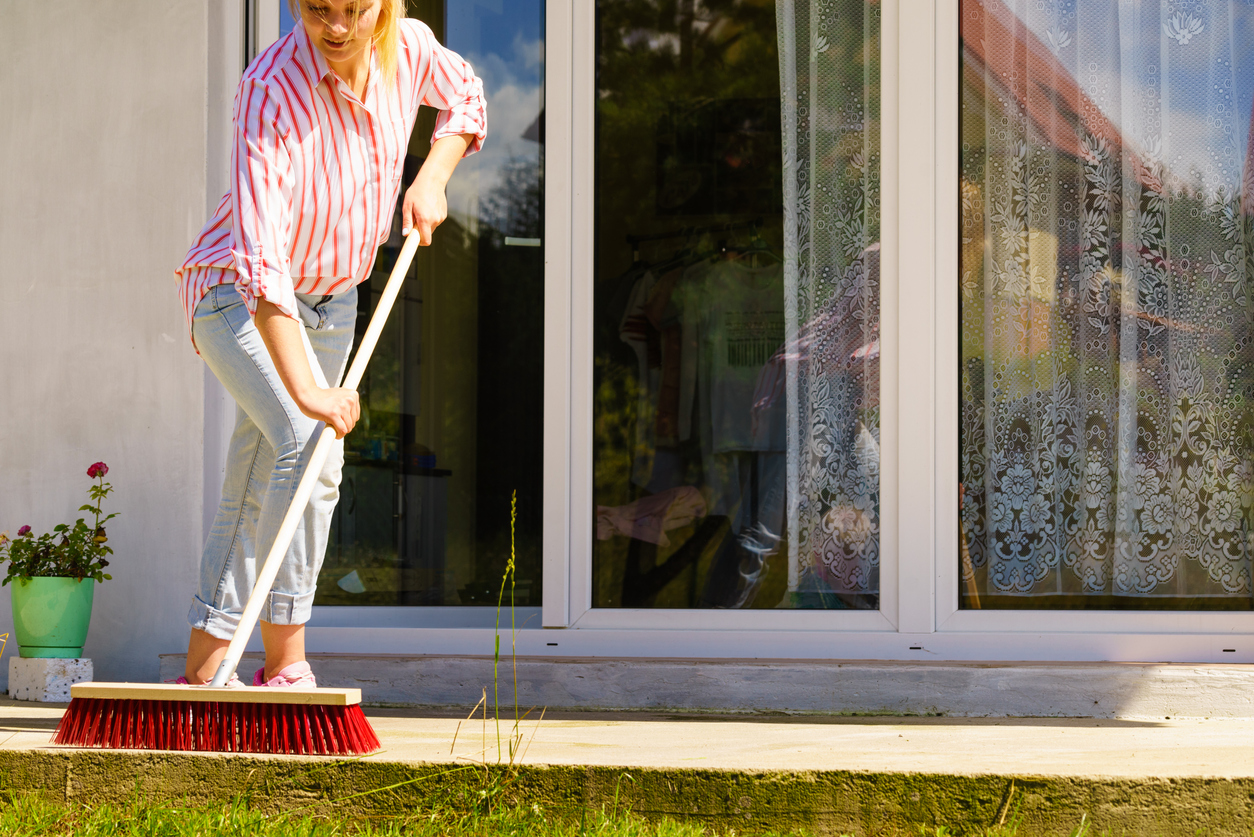 A person sweeping a concrete patio in preparation for cleaning concrete floors and driveways.