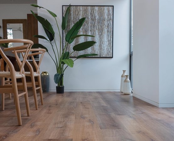 View of the vinyl plank floor and a tall plant in a dining/living space, some dining chairs and