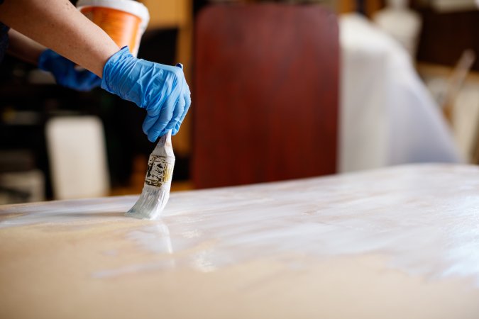 wooden board laying flat, using paintbrush and white paint.