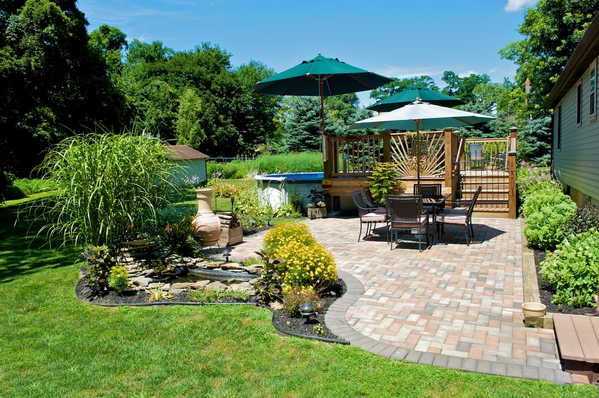 A backyard brick patio with tables under green umbrellas and potted plants.