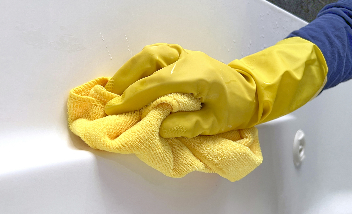 Person wearing rubber gloves uses a microfiber towel to wipe the bathtub.