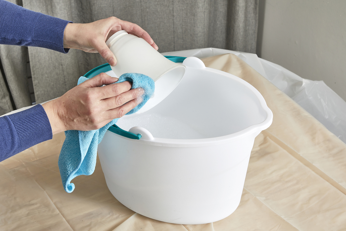 Woman washing glass shades of ceiling fan light fixture in a bucket of soapy water.