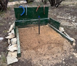 Dark green wooden horseshoe pit surrounded by large stones.