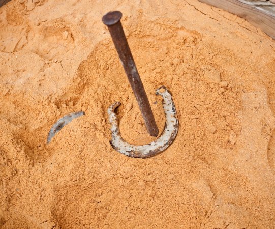 Closeup of a horseshoe around a horseshoe stake and rust-colored sand.