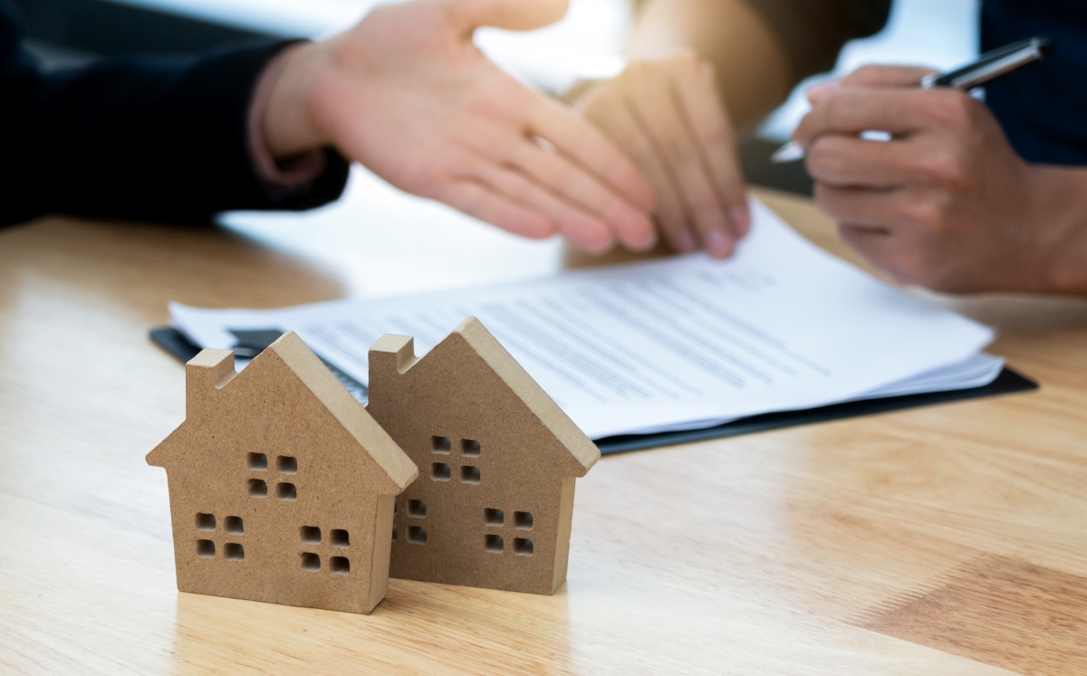 People signing a contract on a table next to two small wooden house models