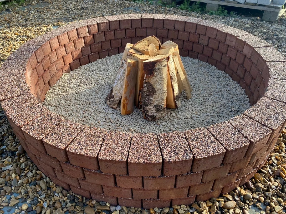 A large fire pit made with bricks filled with smaller stones in the center and a small tower of wood.