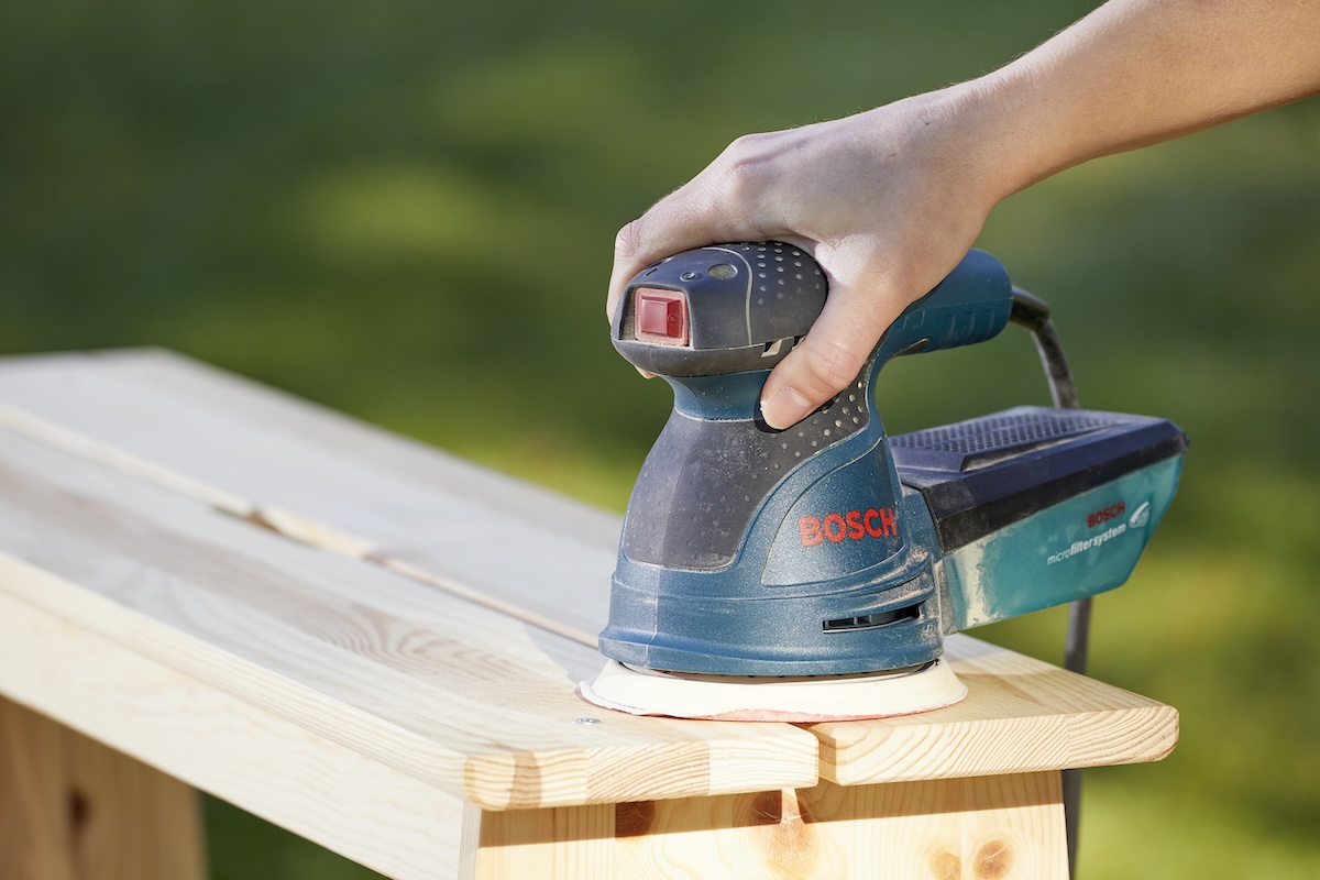 Woman uses a sander on wooden furniture.