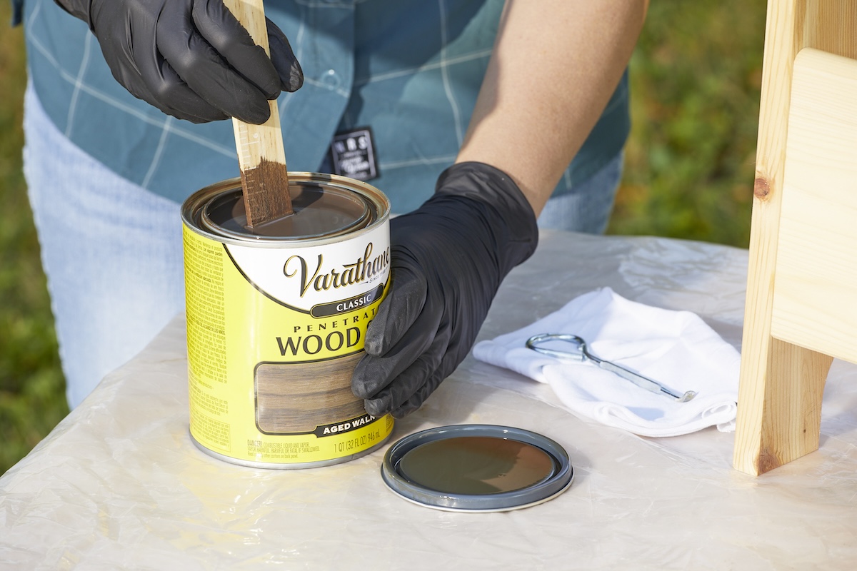 Mixing wood stain before applying it to furniture while wearing rubber gloves.