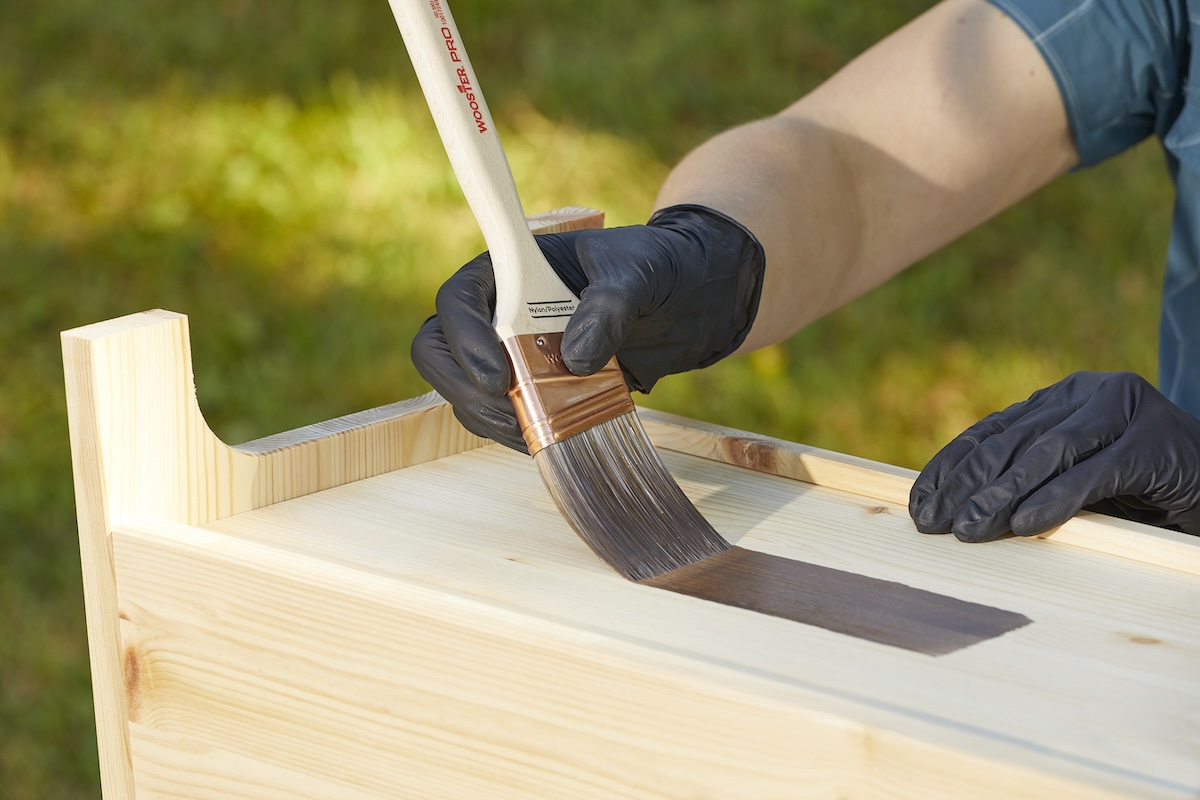 Applying wood stain to furniture with a paintbrush and rubber gloves.