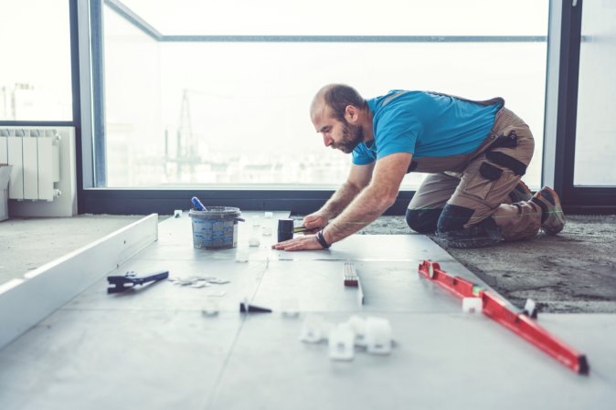 how to install ceramic tile - man installing tile inside building