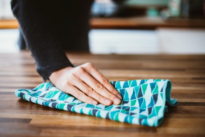 A hand holding a cloth to wipe a wooden countertop