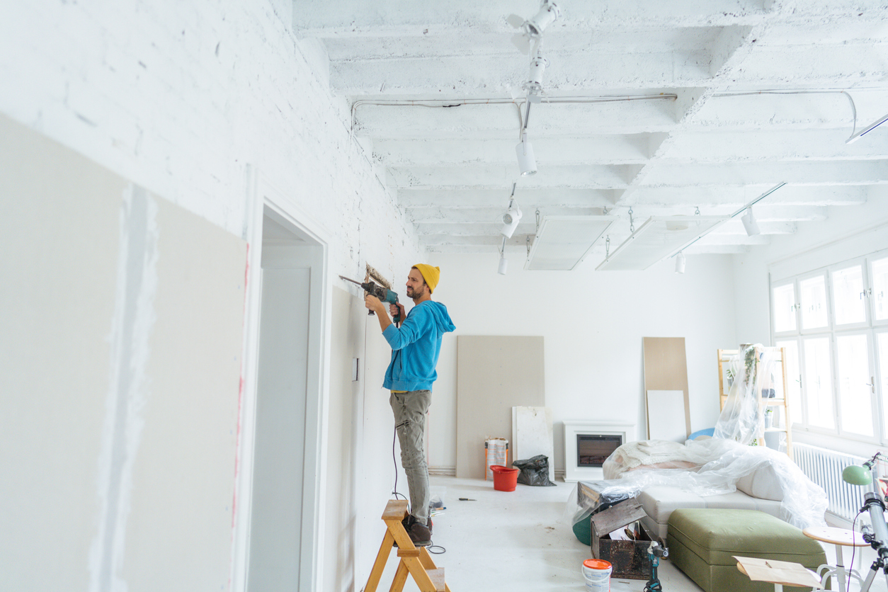 Photo of a young man using a heavy-duty drill machine, drilling through walls, and working on his home remodeling project.