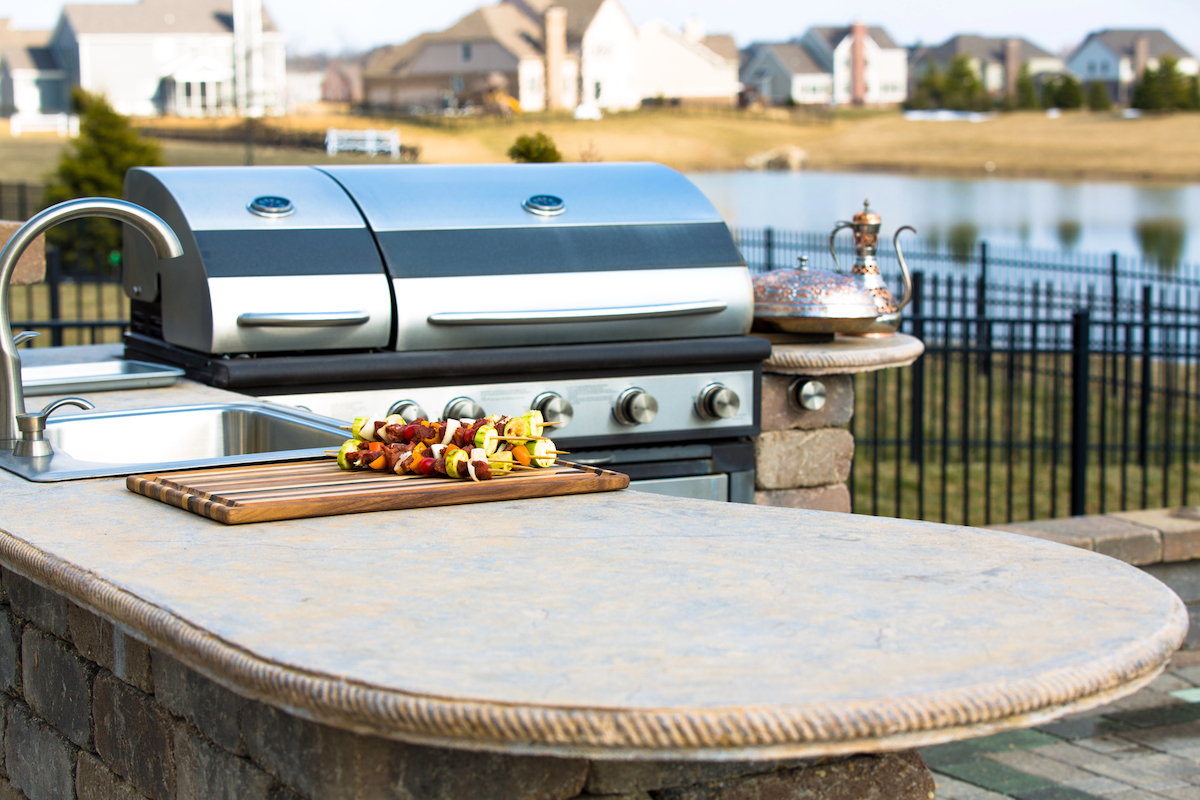 A concrete outdoor kitchen countertop with a stainless steel sink is next to a stainless steel grill.