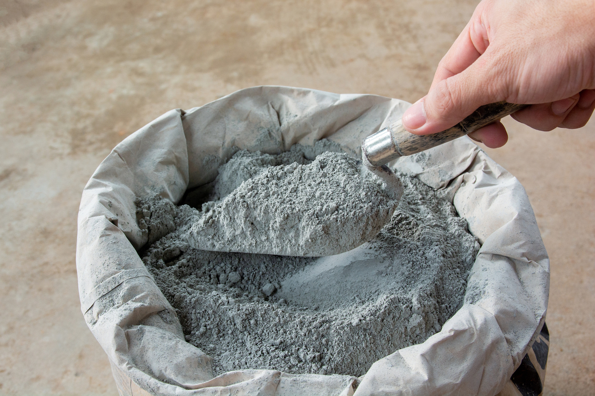 A person is holding a trowel full of cement powder over a bag full of cement powder.