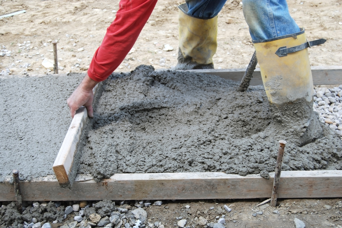 A concrete finisher is leveling wet concrete to make a sidewalk.