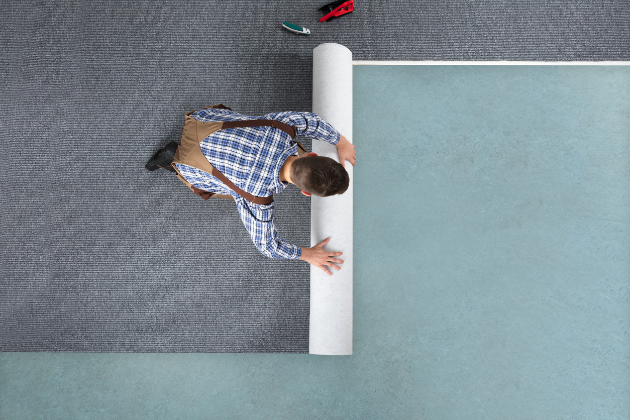 High Angle View Of Young Male Worker In Overalls Rolling Carpet On Floor At Home