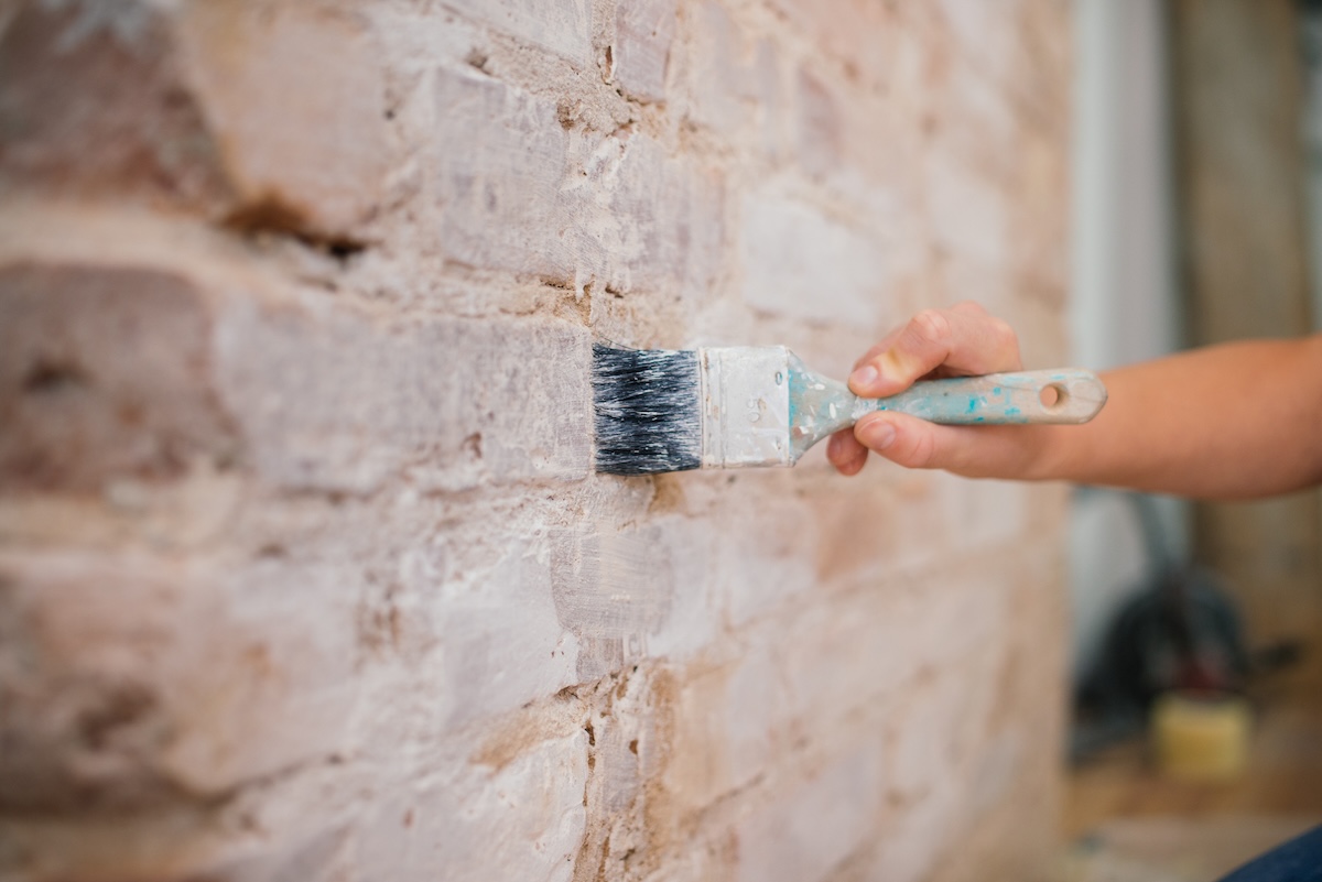 Brick wall being painted with paintbrush. 