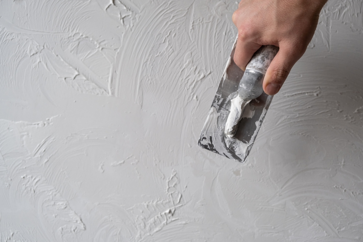 A hand is adding texture to a wall using a trowel.