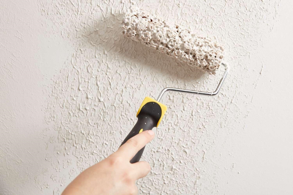 A hand is using a paint roller to add texture to a wall.