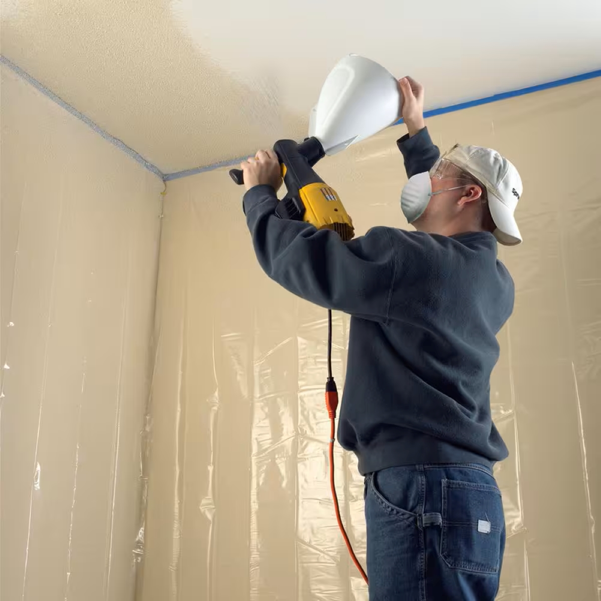 A person is using a texture sprayer on the ceiling.