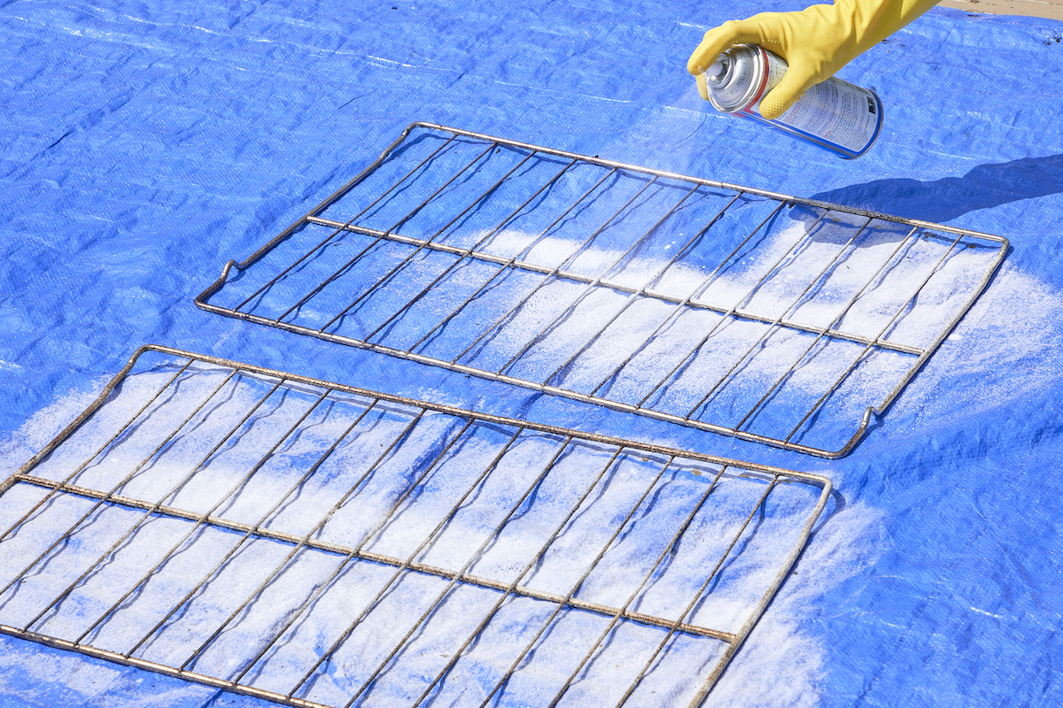 Woman sprays oven racks with oven cleaner on a blue plastic tarp.