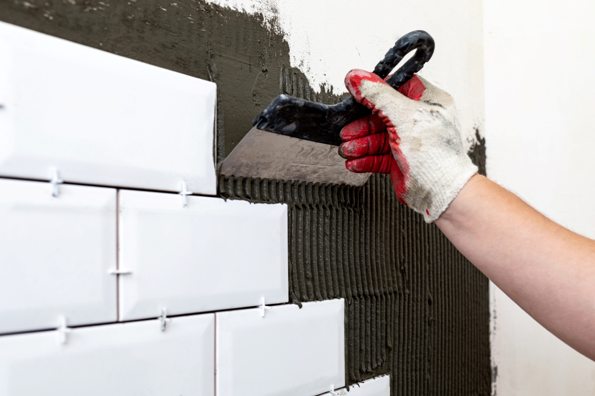 how to tile a bathroom wall - hand adding adhesive on wall for tiling