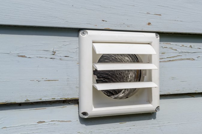 Exterior white vent of a clothes dryer on a house with light blue siding.