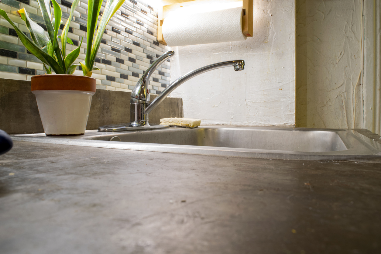 POV shot on cement countertop with sink and plant in background