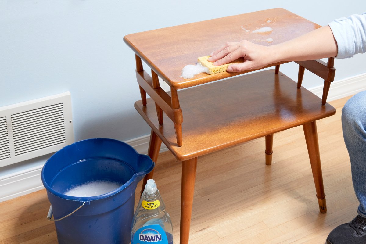 Woman cleans a small wood table with a dish soap and water solution.