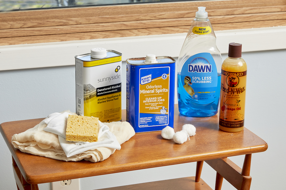 Materials needed to clean wood furniture (including mineral spirits and dish soap) collected on a small wood table.