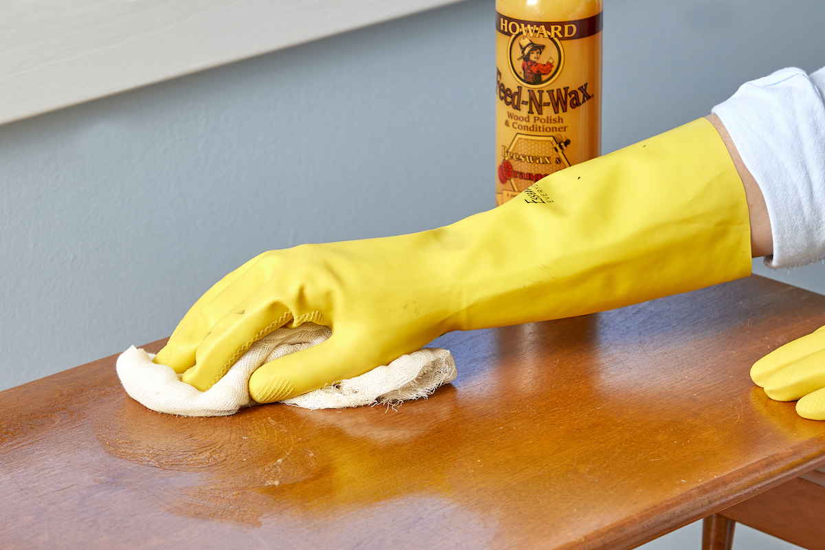 Woman wearing yellow cleaning gloves applies Feed-n-Wax to a wood table. 