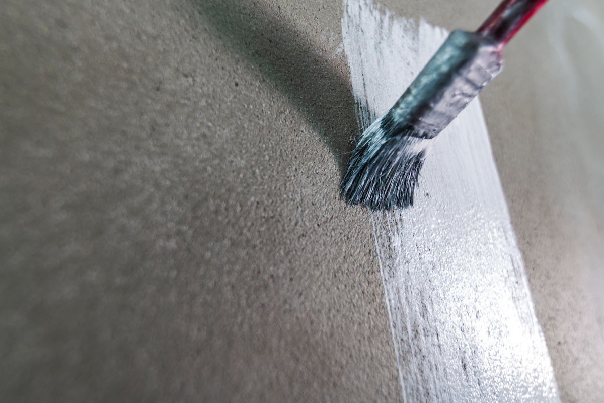 Using paintbrush to paint concrete wall white. 