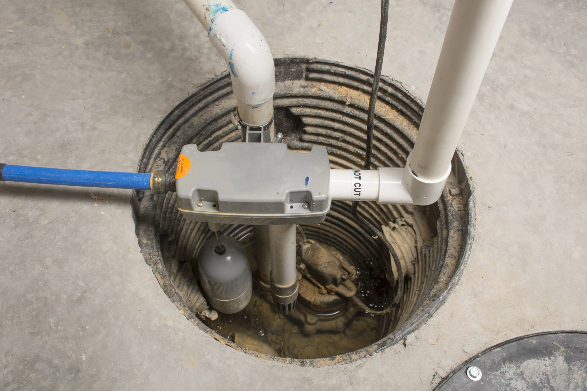 A newly installed sump pump is connected to a hose and pipes in a hole in a home's basement.