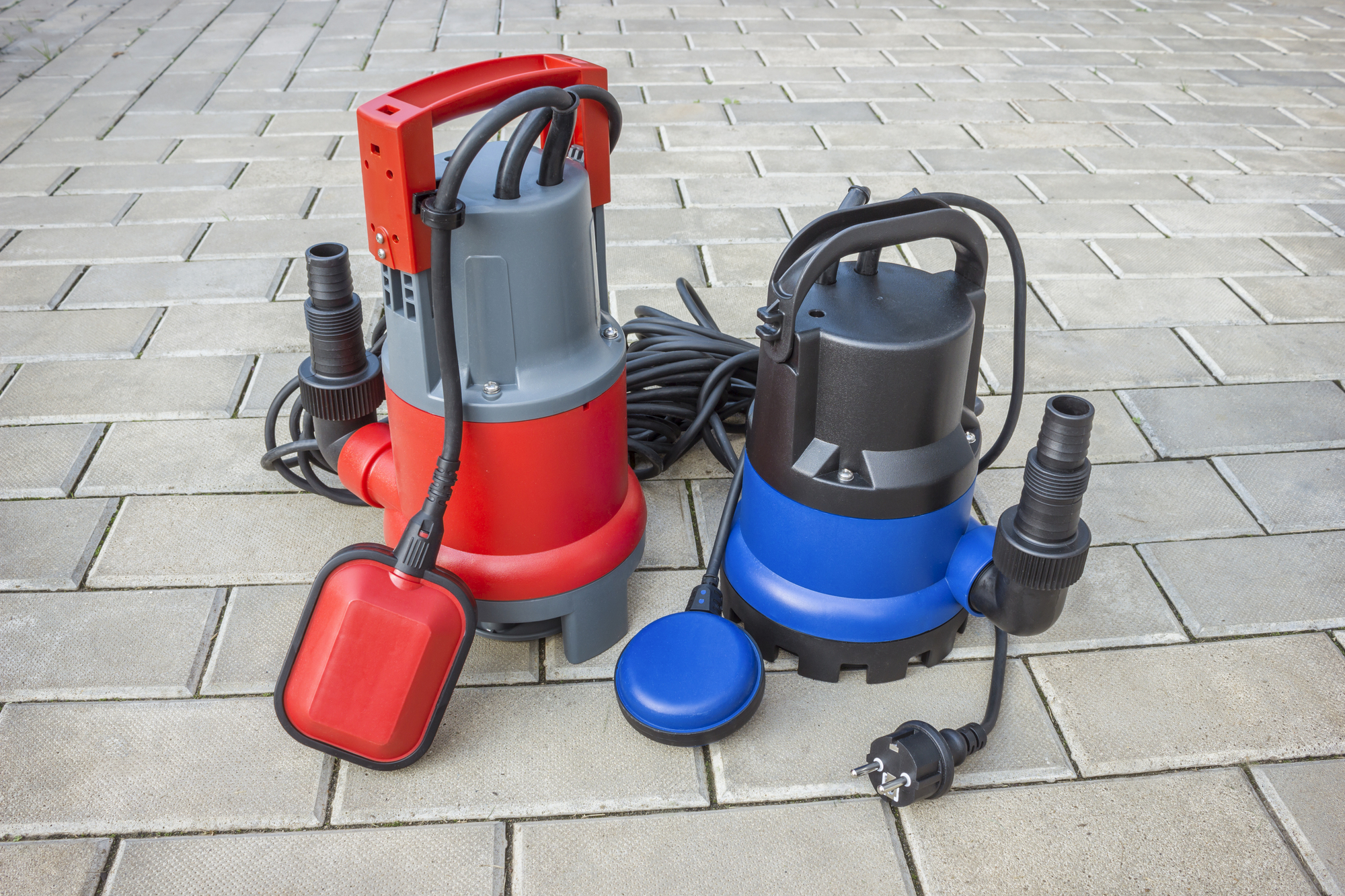 Two new sump pumps (a larger red pump and a smaller blue one) sit on a patio.