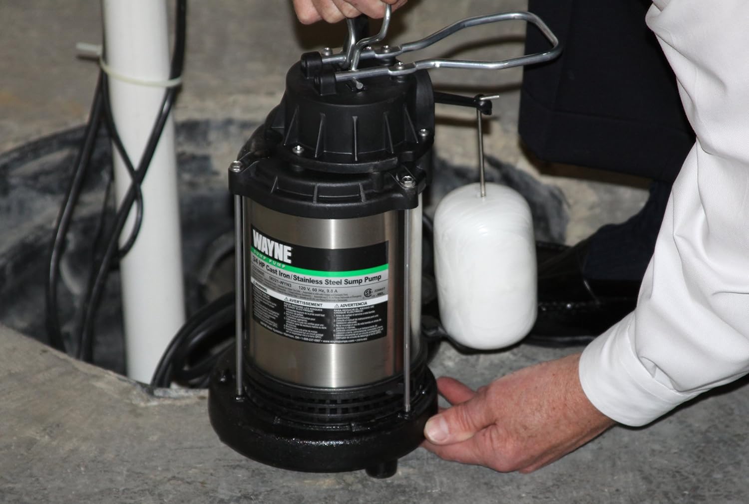 A man lifts a stainless steel Wayne sump pump to place it into a newly-dug sump pit.