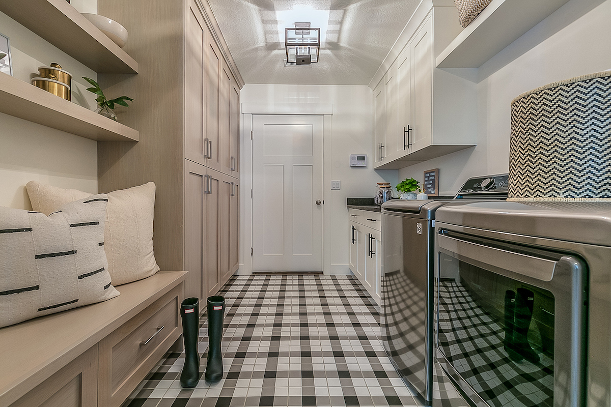 A mudroom with rainboots in the middle of the room features a washing machine and dryer.