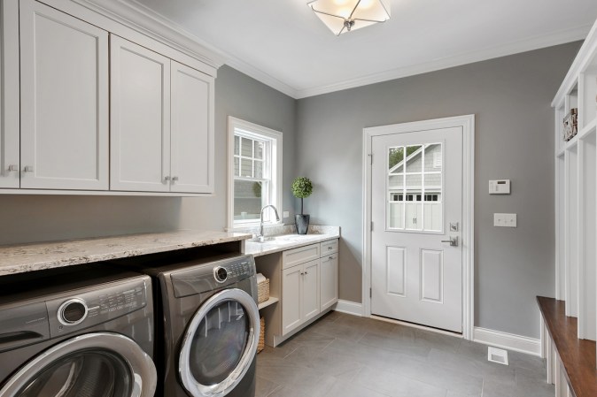 A washing machine and dryer are underneath a counter in a mudroom with a sink.