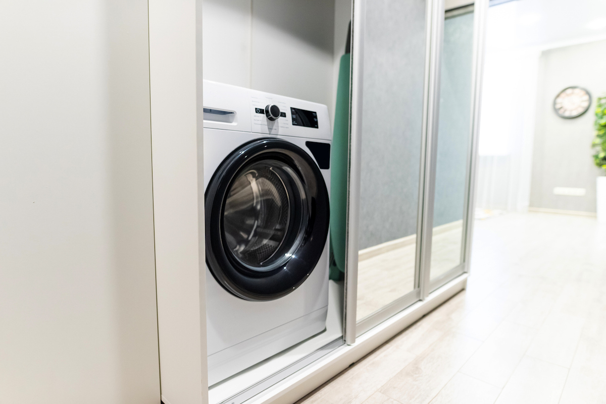 A hallway closet door is half opened revealing a washing machine.