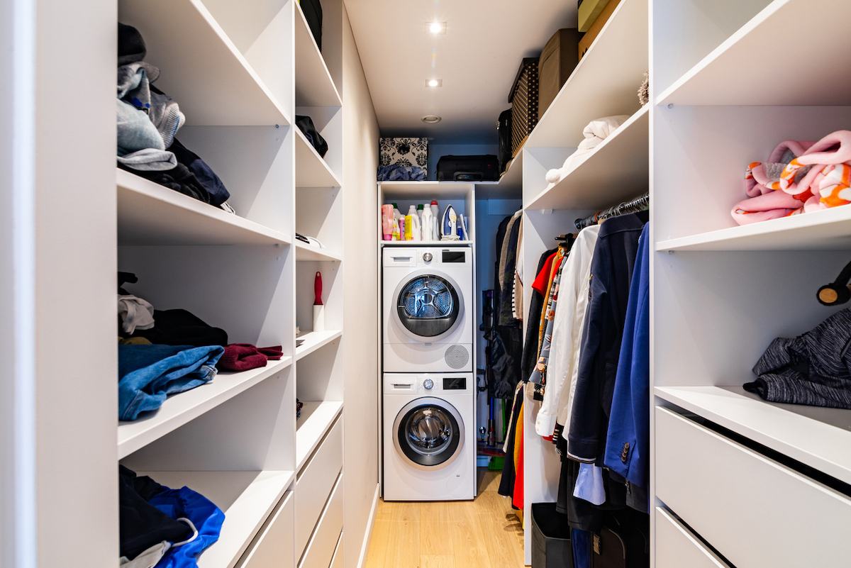 A stackable washing machine and dryer are inside of a walk-in closet.