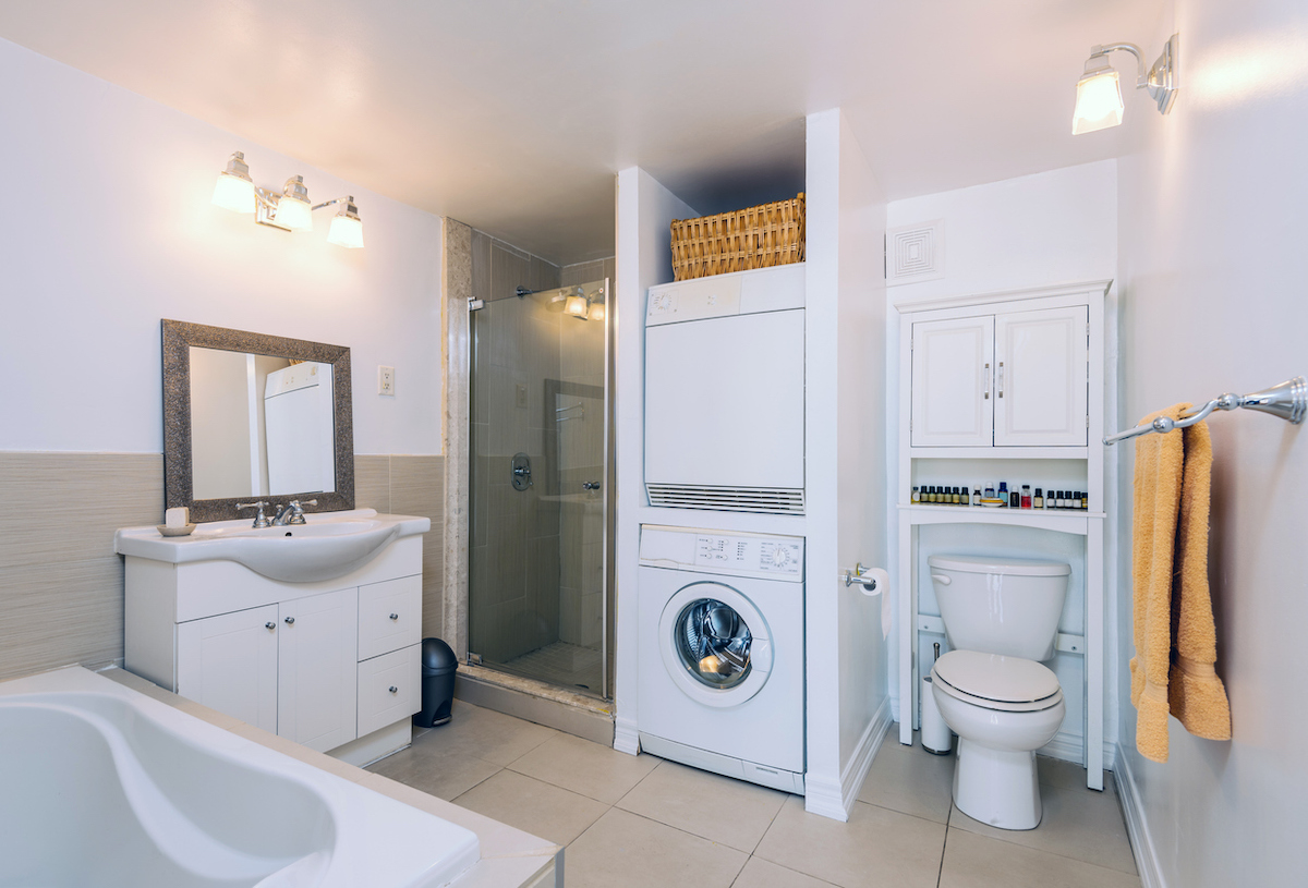 A stackable washing machine and dryer are featured inside a large bathroom.