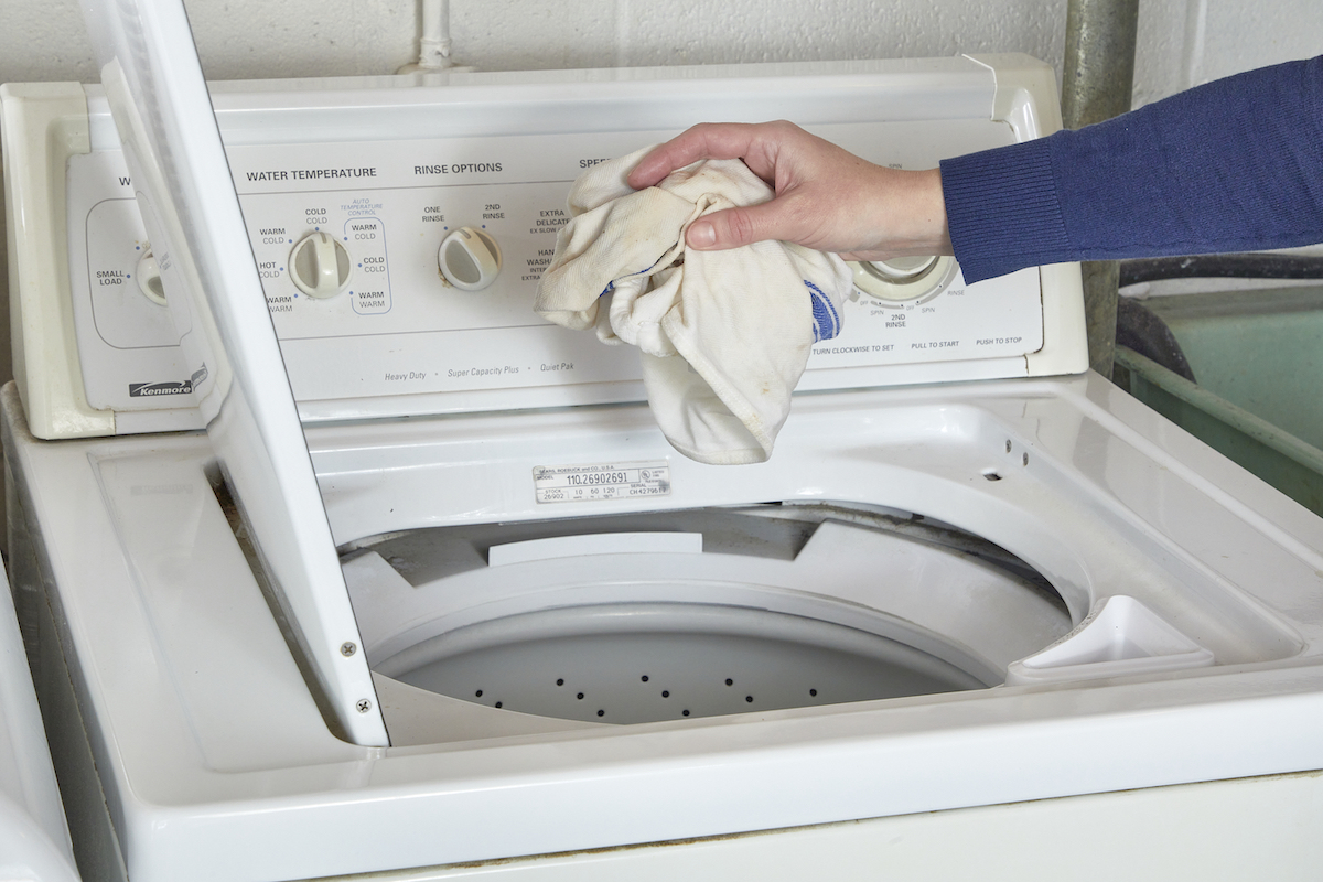 Woman throwing a dishtowel into a top-load washing machine.